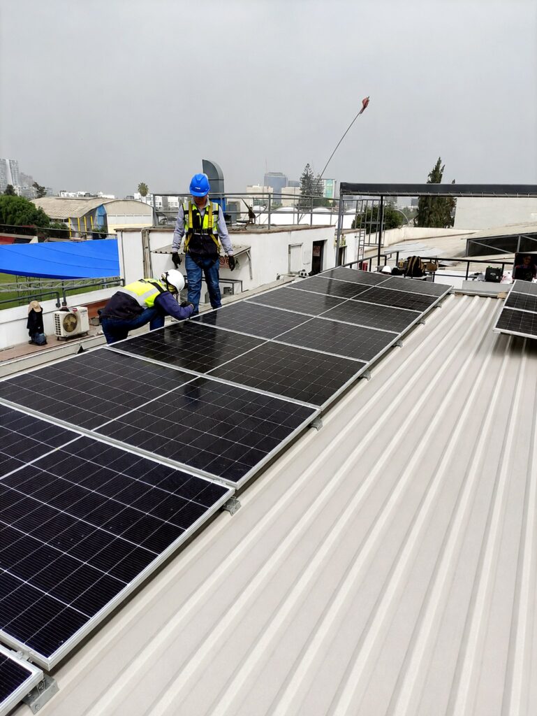 Técnicos de Intelligenio instalando paneles solares sobre techo metálico industrial en Lima
